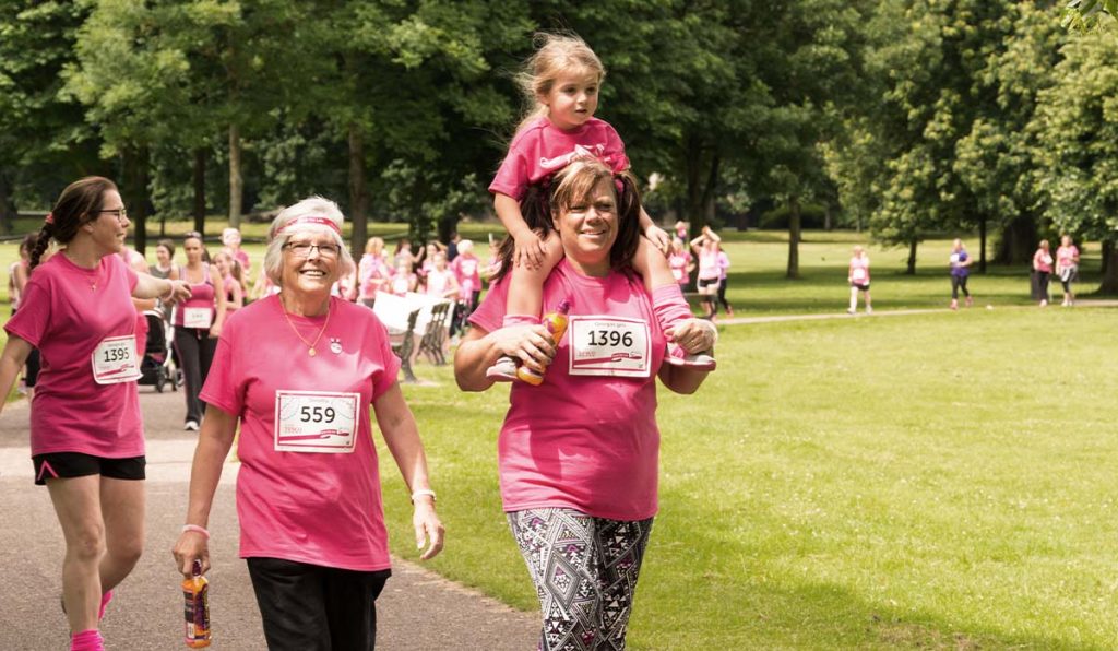 Group of people in pink tshirts and numbers walking around a park.
