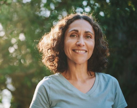 Woman with brown curly hair smiling with trees behind her