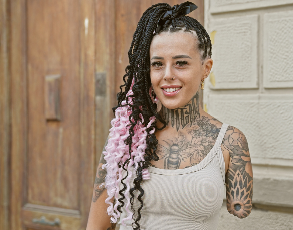 Woman with amputated arm with finely braided black and pink hair and tattoos smiling at camera